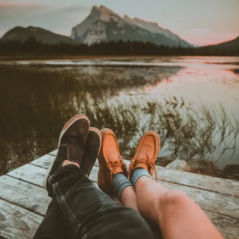 Two pairs of feet on a jetty by a mountain lake